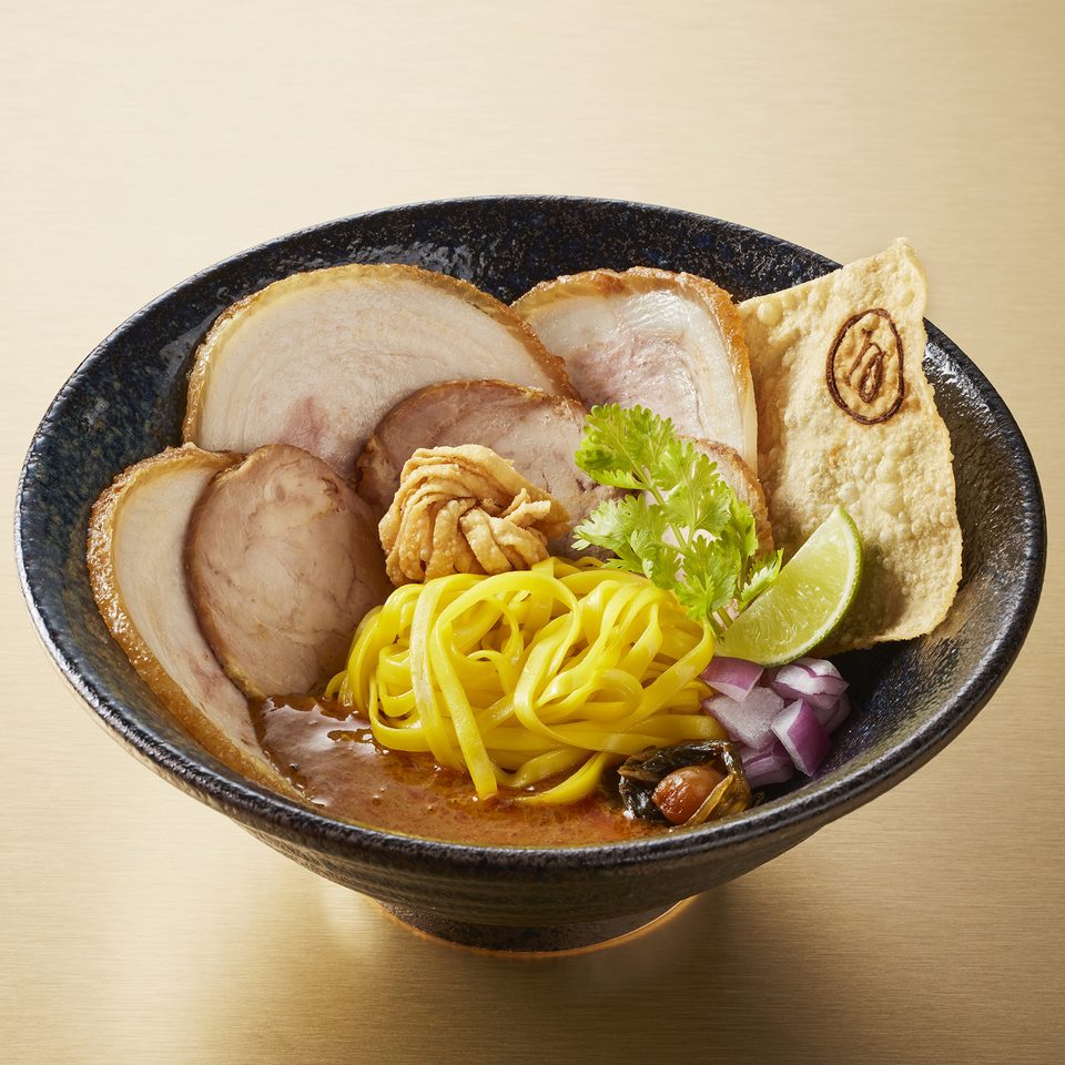 Khao soi with slices of Kurobuta chashu, egg noodles, a crisp wonton sheet and lime