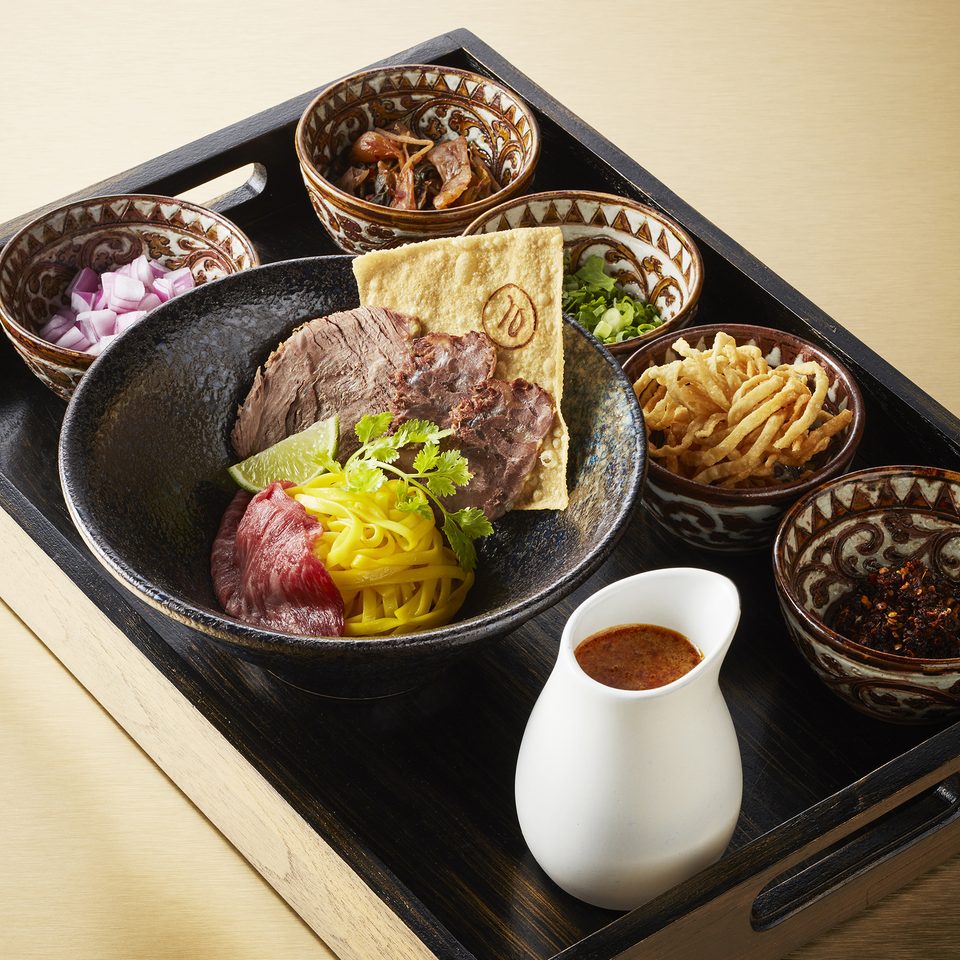 Khao soi with sliced wagyu and braised beef, on a tray of condiments