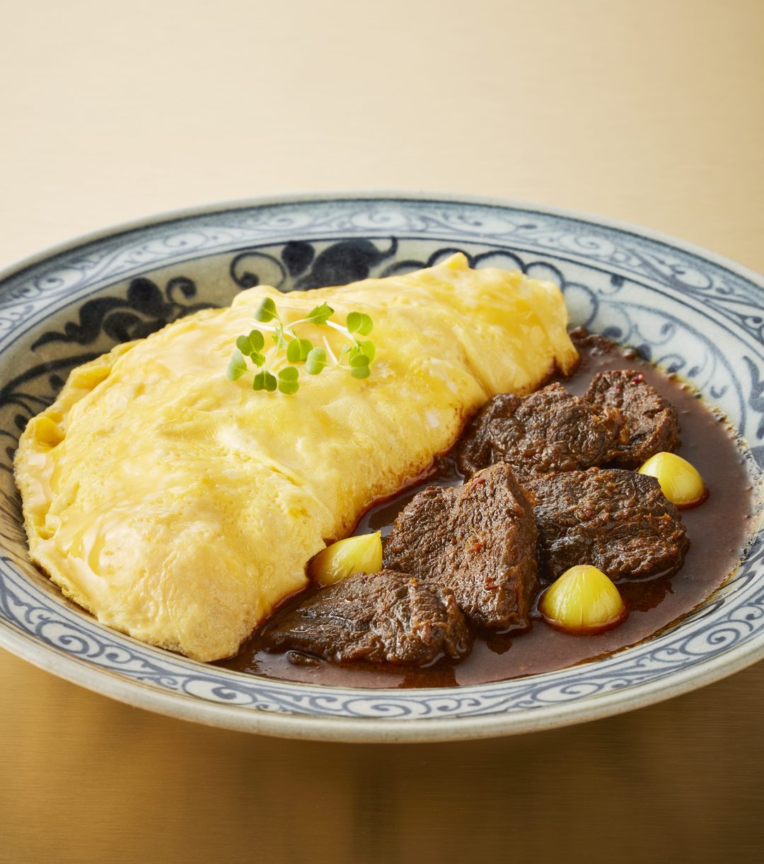Hung lae curry with braised beef cheek beside a soft omelette, in a blue-and-white bowl